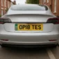 Rear view of an electric car with UK legal yellow number plate displaying OP18 TES and a green EV identifier