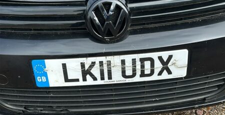 Front view of a black Volkswagen with a UK registration plate displaying "LK11 UDX," showing visible scratches and cracks on the plate.