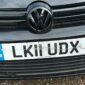 Front view of a black Volkswagen with a UK registration plate displaying "LK11 UDX," showing visible scratches and cracks on the plate.