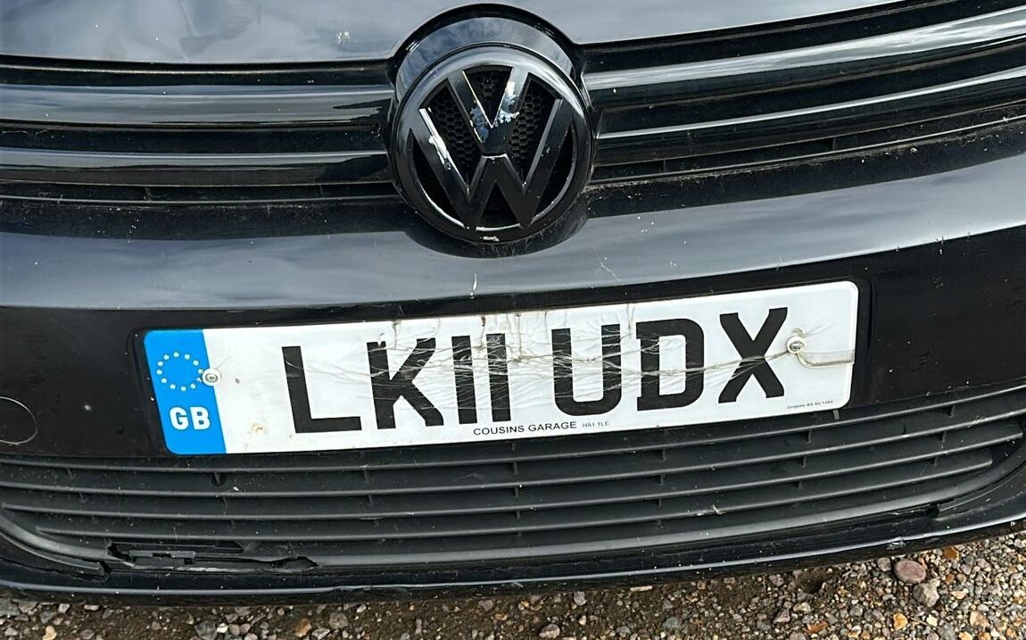 Front view of a black Volkswagen with a UK registration plate displaying "LK11 UDX," showing visible scratches and cracks on the plate.